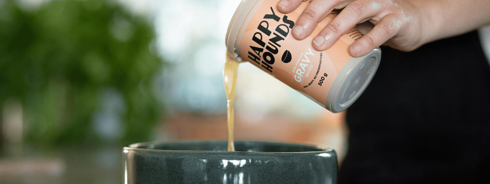 Happy Hounds fresh gravy treat being poured into a dark moss green dog bowl.