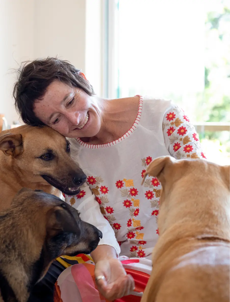 Emma, the founder of Happy Hounds, smiling and cuddling with her pack of rescue dogs