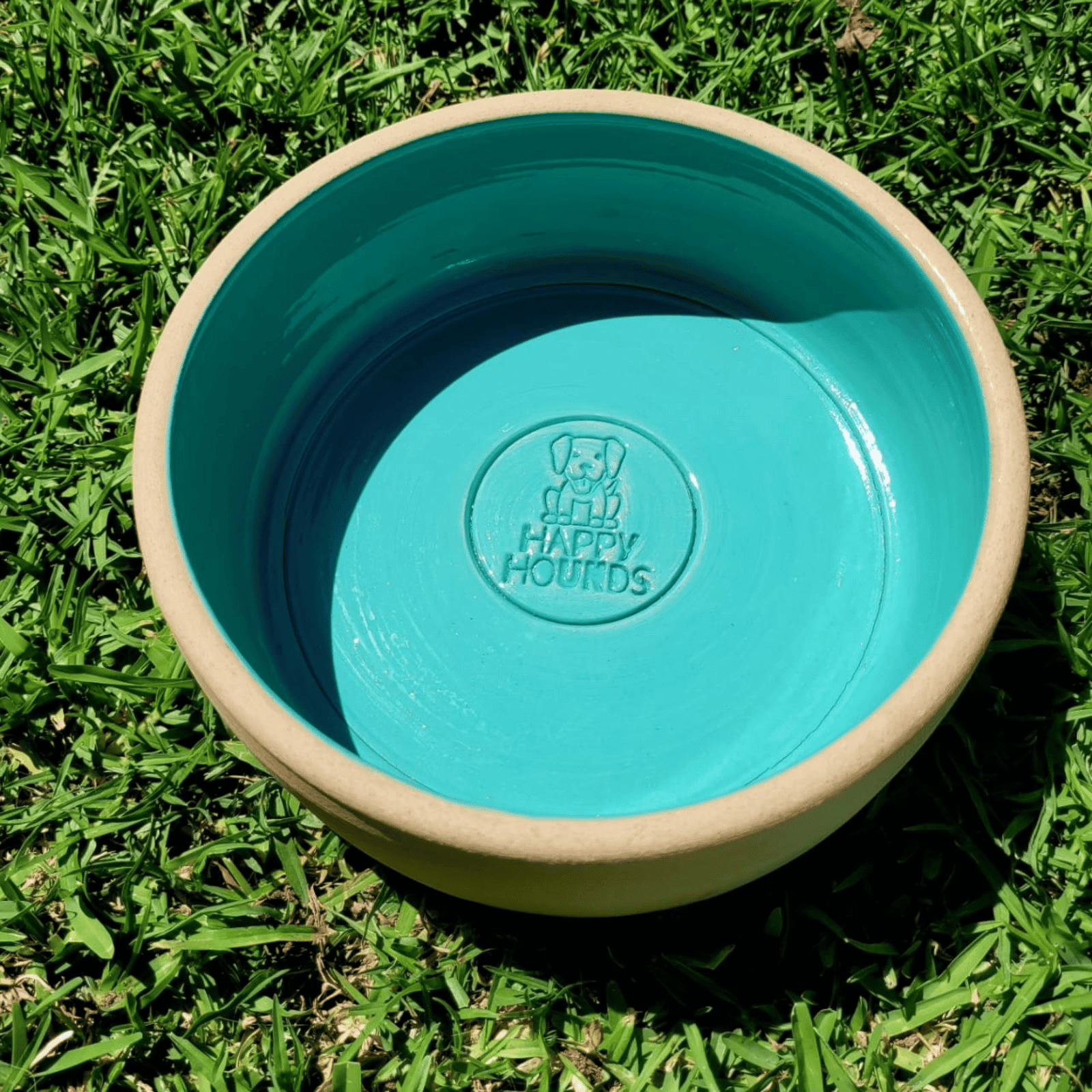 A light blue glazed ceramic Happy Hounds bowl on green grass