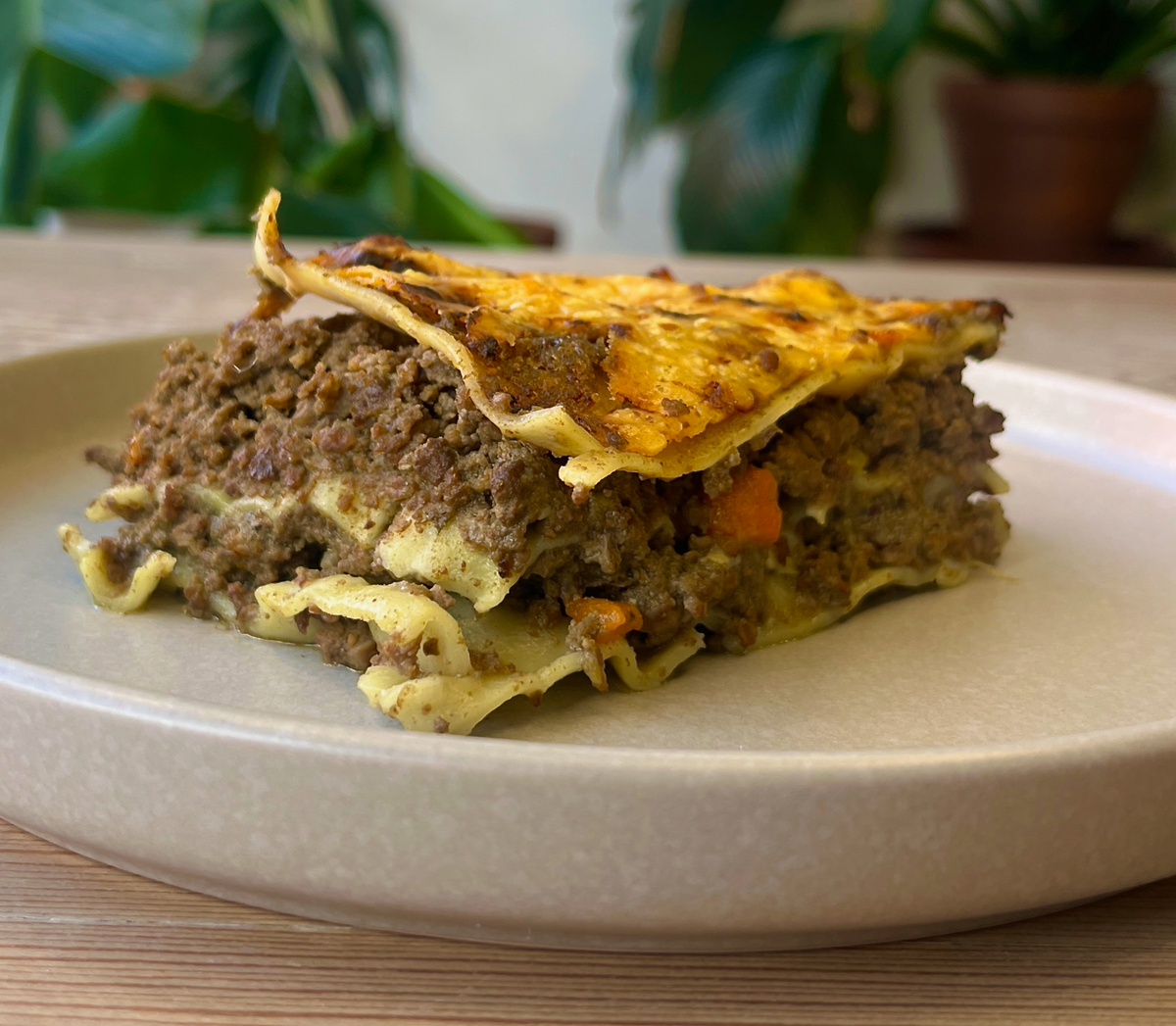 Slice of lasagna on a beige plate with a blurred background